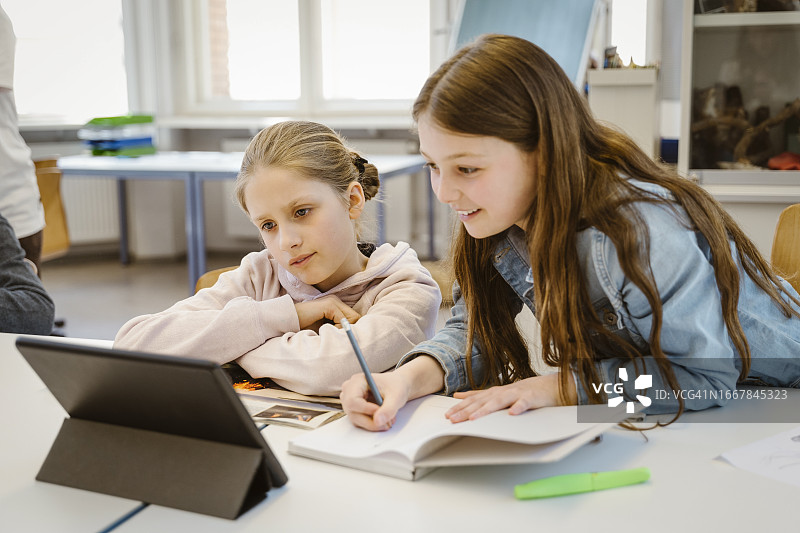 好奇的女学生坐在课桌前通过平板电脑进行电子学习图片素材