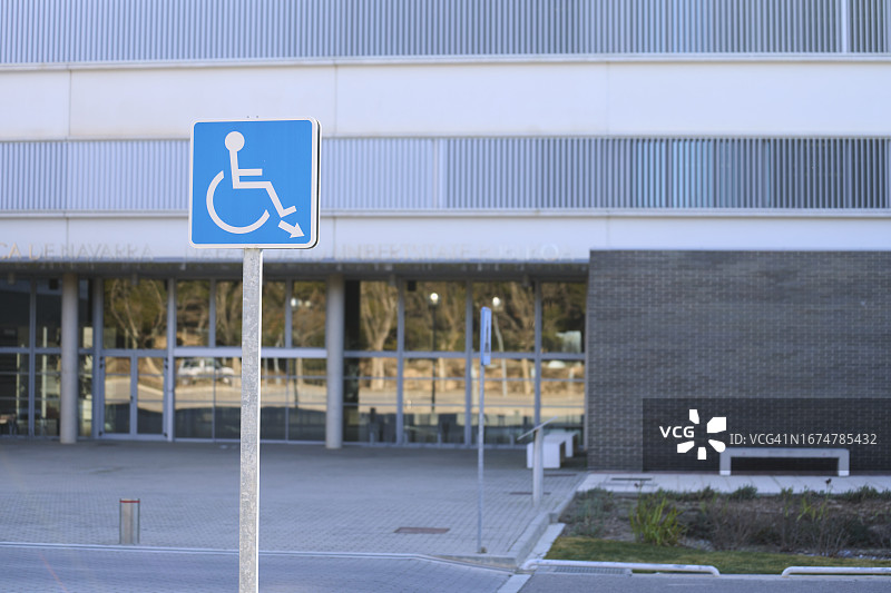 一个有玻璃门的大楼外停车场的残疾人标志特写。图片素材