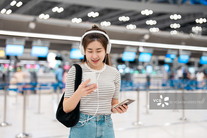 一名亚洲年轻女子在机场候机楼等候时使用手机。图片素材