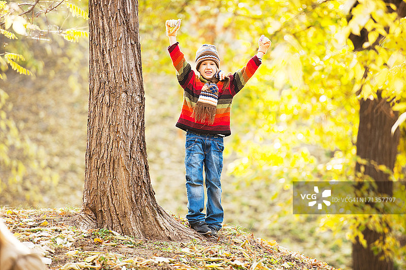 可爱的男孩高举着手臂站在森林里。图片素材
