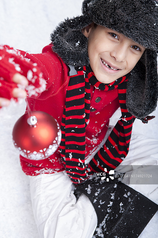 小男孩坐在雪地里，手里拿着圣诞小玩意儿图片素材