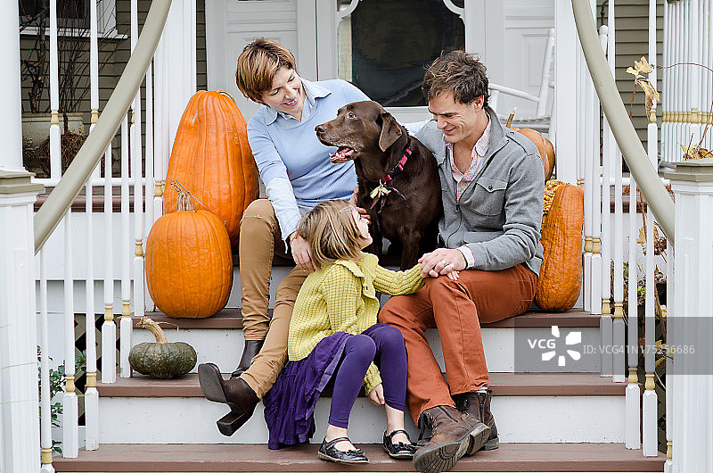与拉布拉多寻回犬一起坐在门廊楼梯上的幸福家庭图片素材