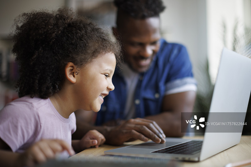 微笑的父亲和他可爱的女儿在家里使用笔记本电脑图片素材