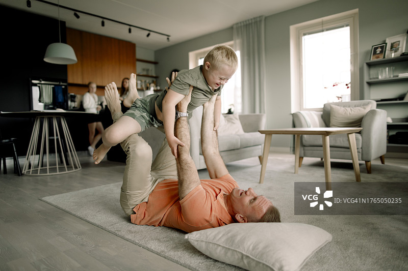 父亲全身躺在地毯上，把儿子抱在家里的客厅里图片素材