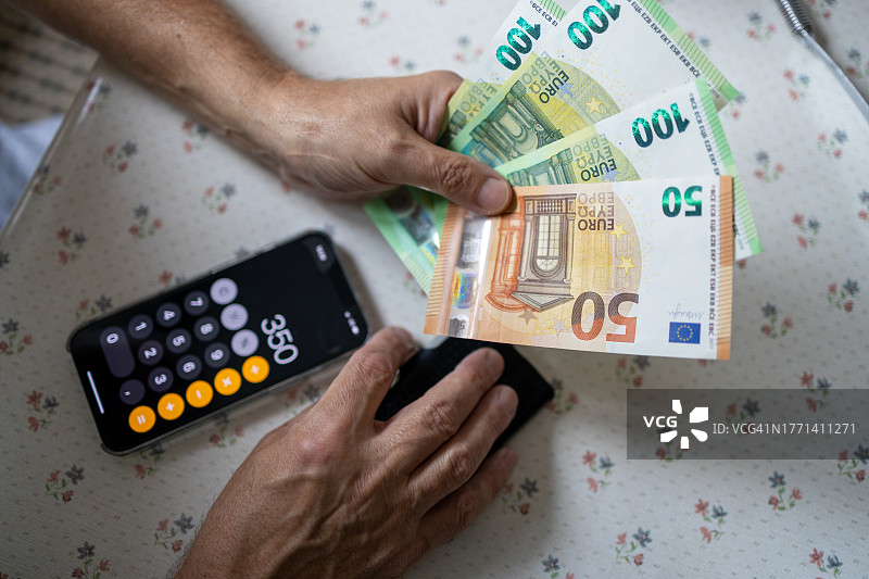 老年人拿着计算器数钱的特写，欧盟钞票图片素材