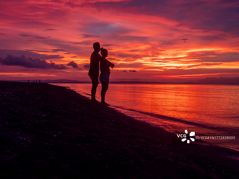 黄昏时分，在壮观的天空下，海滩上一对夫妇的剪影图片素材