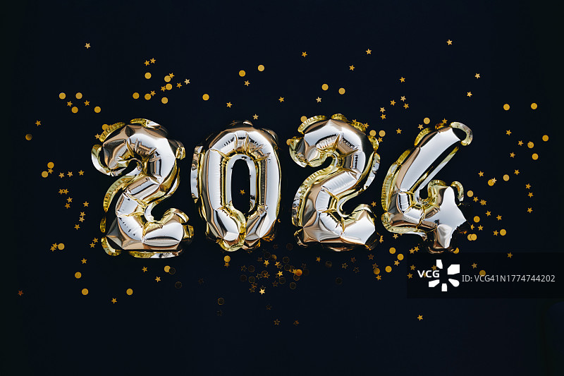 2024年新年贺卡。在黑色的背景上用金色的五彩纸屑衬托金色的气球图片素材