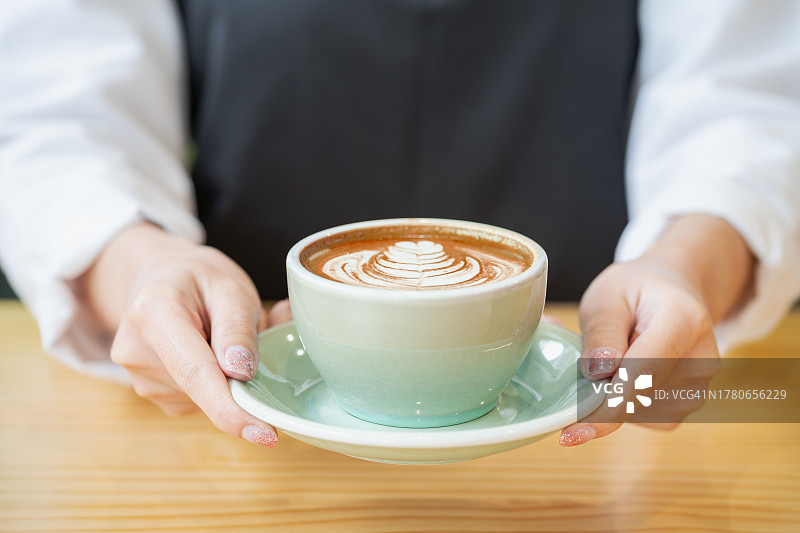 在咖啡厅柜台为顾客端上一杯咖啡的亚洲咖啡师或女服务员。咖啡店特许经营和销售点(POS)解决方案的小企业概念。图片素材