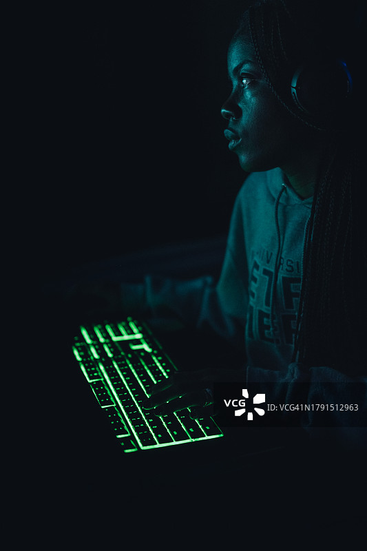 美国德克萨斯州科珀斯克里斯蒂，一名年轻女子在暗室里用发光的键盘玩游戏，同时把目光移开图片素材