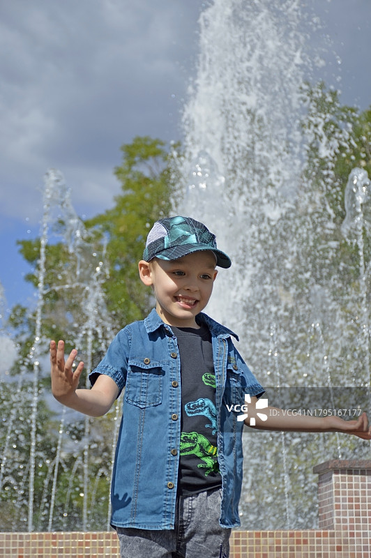 微笑的男孩站在喷泉旁的肖像图片素材