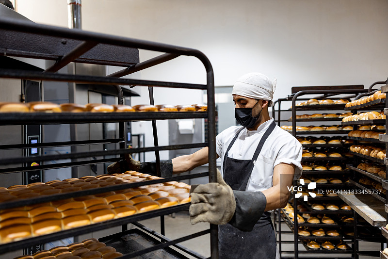 在一家工业面包店，面包师正在搬运一排面包托盘图片素材