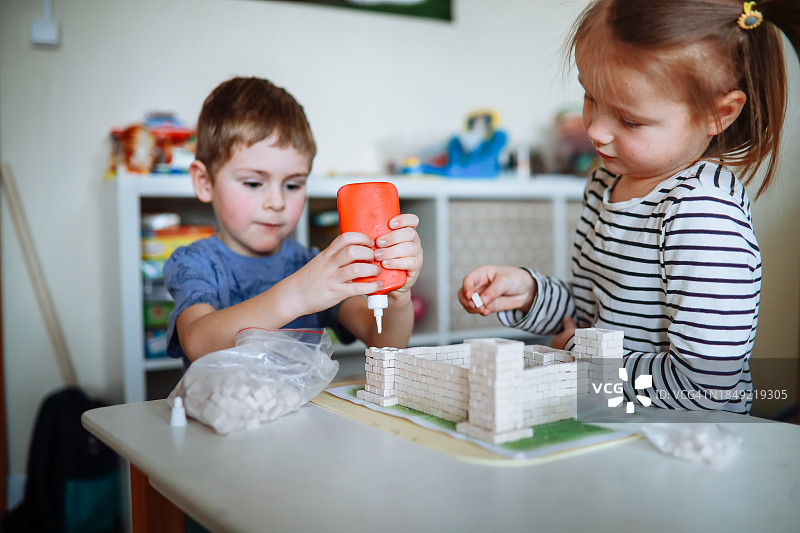 创意建筑:男孩和女孩在孩子们的房间里用小砖块和胶水合作创建一个玩具城堡。图片素材