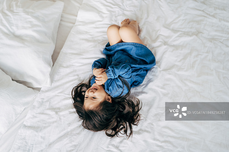 可爱的亚洲小女孩开心地笑着躺在床上，她的熊猫毛绒玩具躺在她旁边图片素材