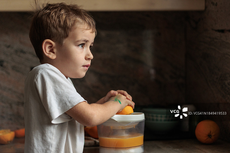 可爱的小男孩在做新鲜的橙汁，然后看向别处图片素材