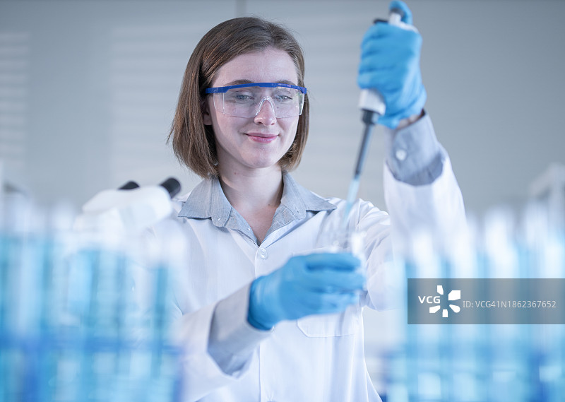 戴着防护眼镜在实验室用移液器工作的女科学家图片素材