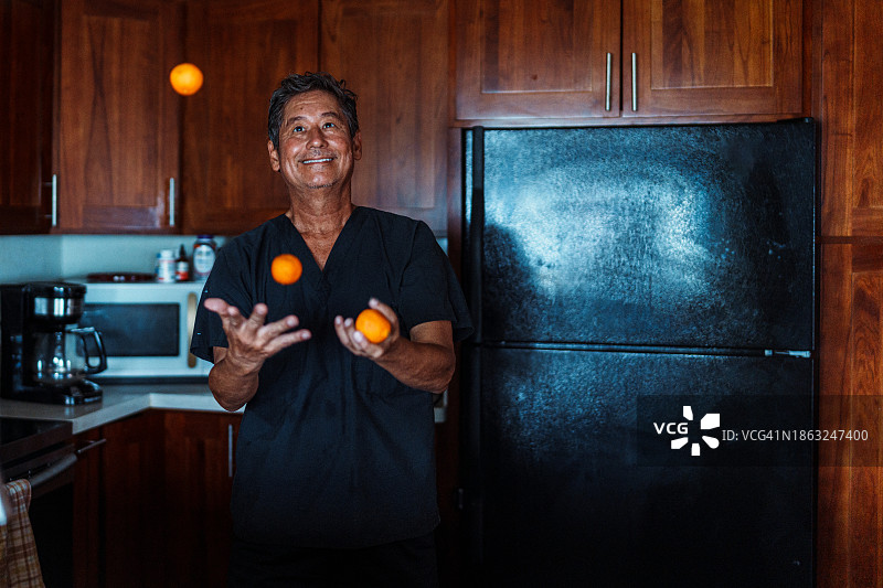 充满活力的夏威夷成年男子在家厨房里摆弄橘子图片素材