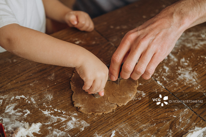 快乐的家庭，爸爸和儿子在厨房。爸爸和儿子在厨房餐桌上做饼干的手图片素材
