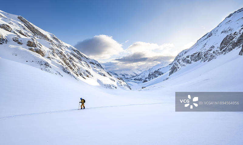 滑雪游客在未受破坏的新鲜积雪中攀登，蓝天白云，白雪覆盖的山脉景观，在瑞士，欧洲伯尔尼阿尔卑斯山的野生角滑雪之旅图片素材