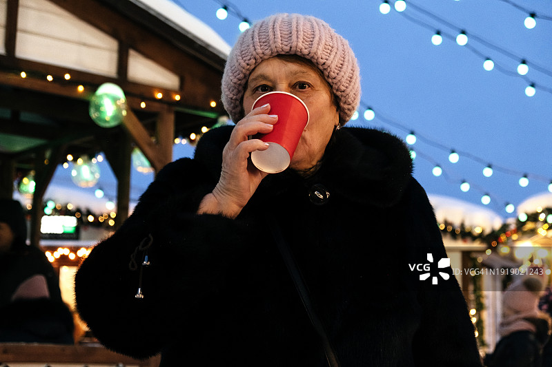 成年女性在圣诞市场喝咖啡。图片素材