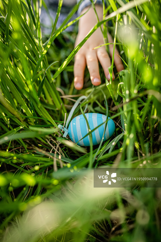 复活节快乐。一个女孩在草地上发现了一个复活节彩蛋。孩子向躺在草地上的复活节彩蛋伸出手。图片素材