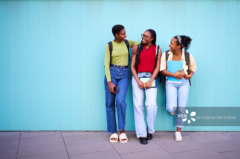 课后，三个黑人女学生朋友站在一个黑人学生旁边聊天。图片素材