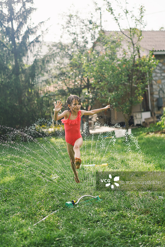 一个小女孩在炎热的夏天跳过花园的洒水装置图片素材