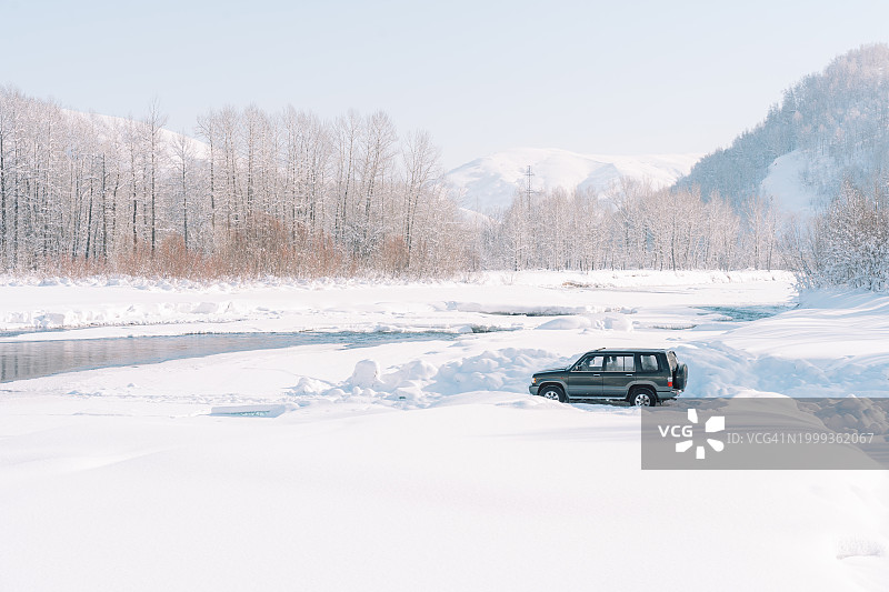 大型越野车行驶在白雪皑皑的河岸上，对面是山林图片素材