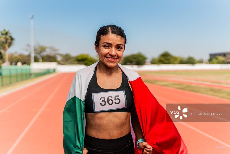中年成年运动员妇女在运动跑道上手持墨西哥国旗的肖像图片素材