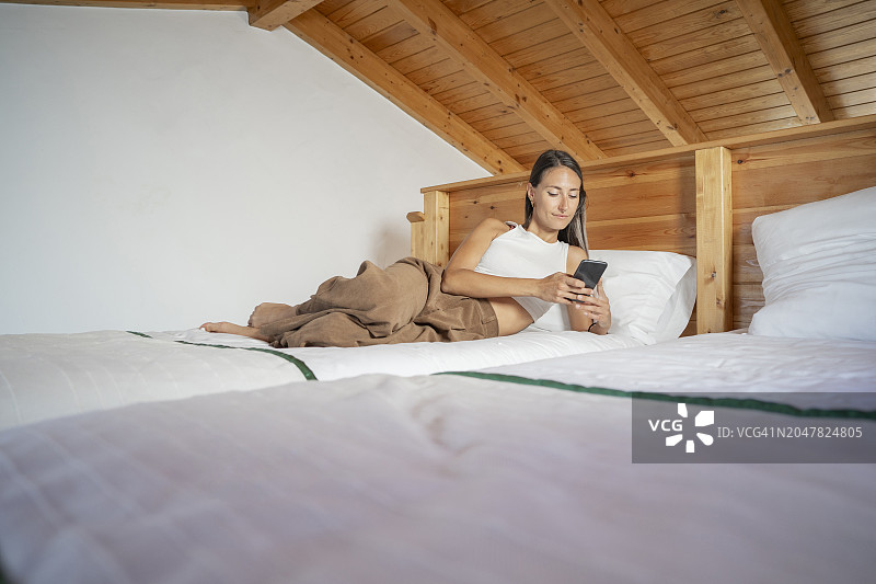 年轻女子躺在床上，在家用智能手机图片素材
