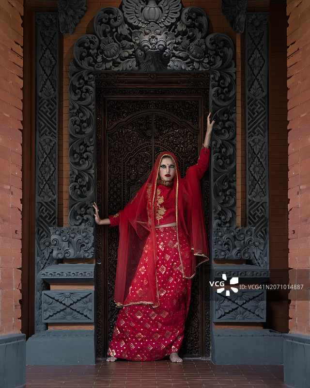 一个穿着印度红衣服的女孩，一扇雕花门的背景是金子图片素材