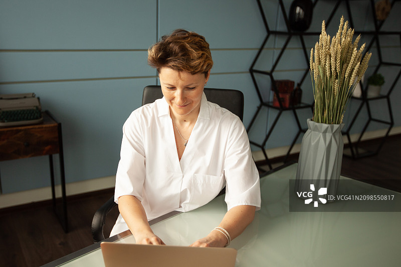 一位身穿白大褂的女医生坐在办公桌前，用笔记本电脑工作图片素材