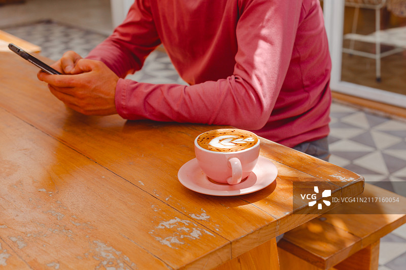 一名男子坐在木桌边喝咖啡，手里拿着智能手机图片素材
