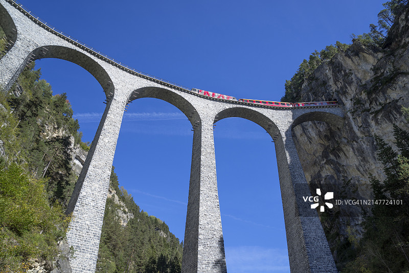 红色火车行驶在瑞士阿尔卑斯山的石质高架桥上。图片素材