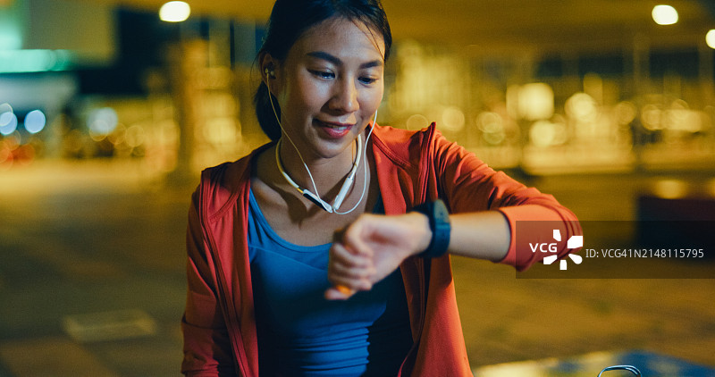 年轻的亚洲女运动员跑步者在城市夜间户外运动前，在智能手表上检查进度并查看智能手表心率监测器。健康的锻炼。图片素材