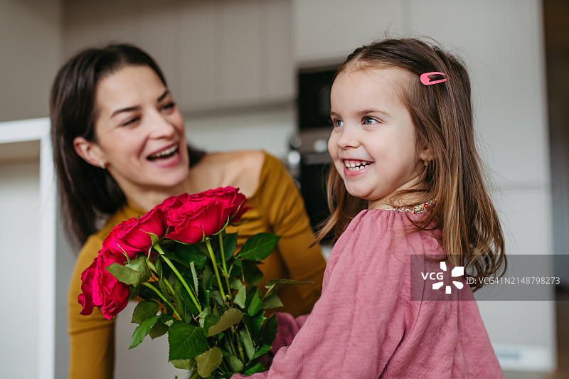 小女儿给母亲送花束的肖像，为母亲节或生日准备的红玫瑰。母亲节和母爱的概念。图片素材