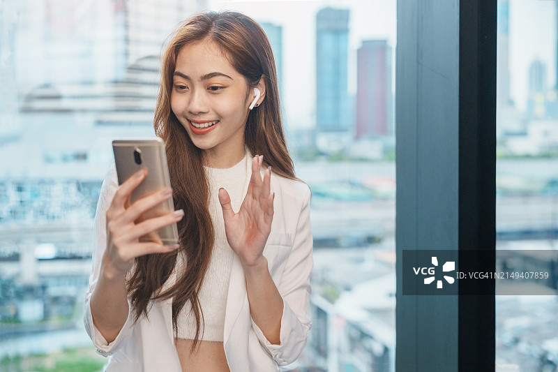 手持智能手机的亚洲女性站在街道模糊的建筑背景下。时尚商务照片的漂亮女孩在休闲套房与手机和一杯咖啡图片素材