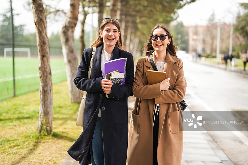 两个女学生拿着笔记本去大学校园上课图片素材