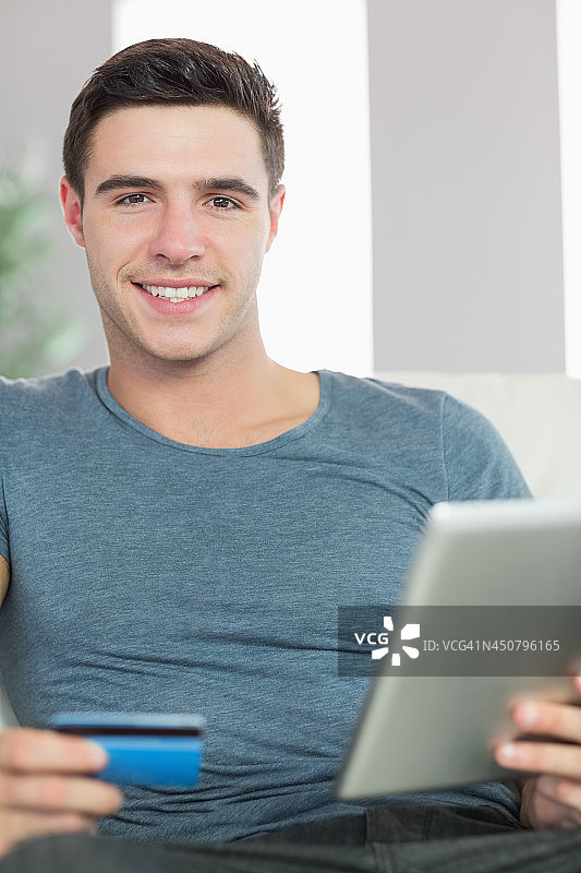 开朗英俊的男人放松在沙发上用平板电脑在网上购物图片素材