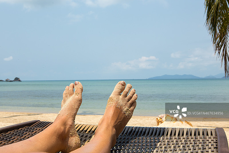女人的脚在热带海滩度假的太阳椅上图片素材