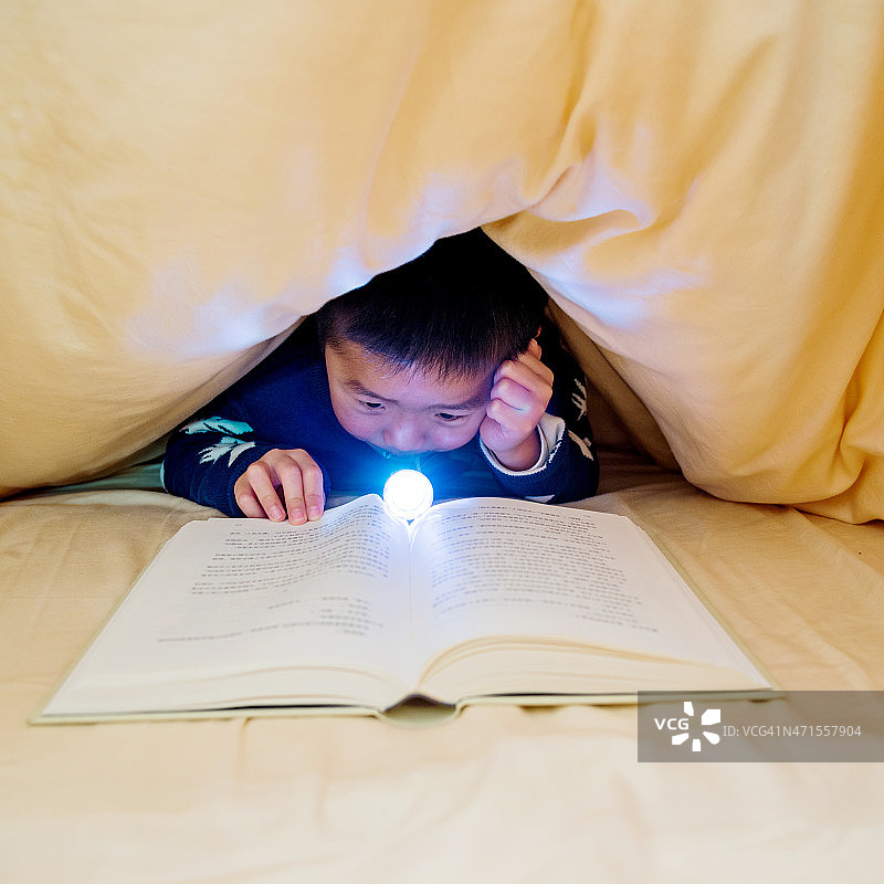 小男孩藏在被窝里看书图片素材