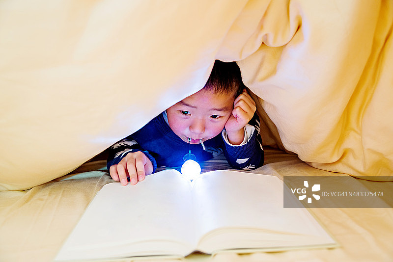 小男孩藏在被窝里看书图片素材