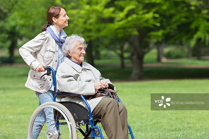 坐在轮椅上的老年妇女和家庭护工在公园里图片素材