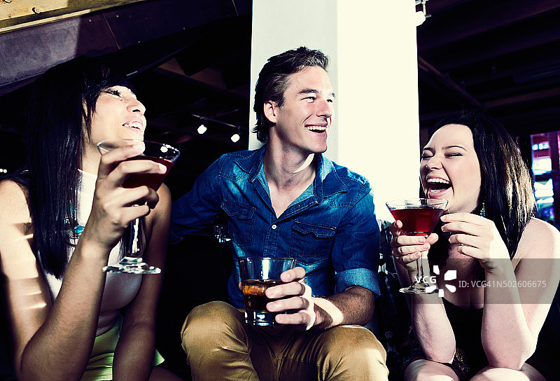 三个年轻人晚上在俱乐部喝酒大笑图片素材