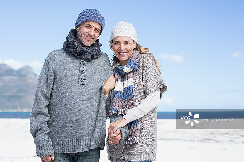 微笑的夫妇站在海滩上，穿着暖和的衣服图片素材
