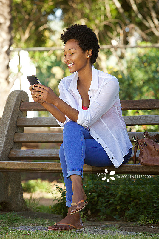 年轻的女士在公园长椅上放松和使用手机图片素材
