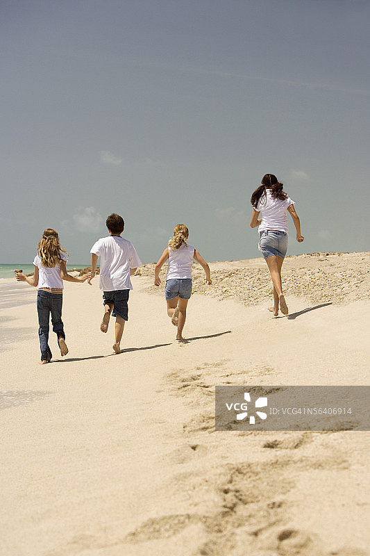 一个男孩和三个女孩在海滩上跑步的后视图图片素材