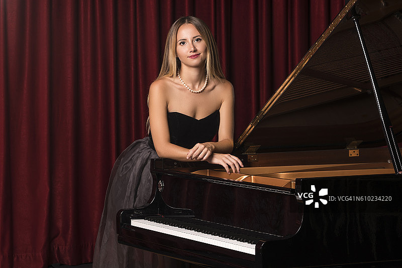 美丽的年轻女性的肖像倚在钢琴上图片素材