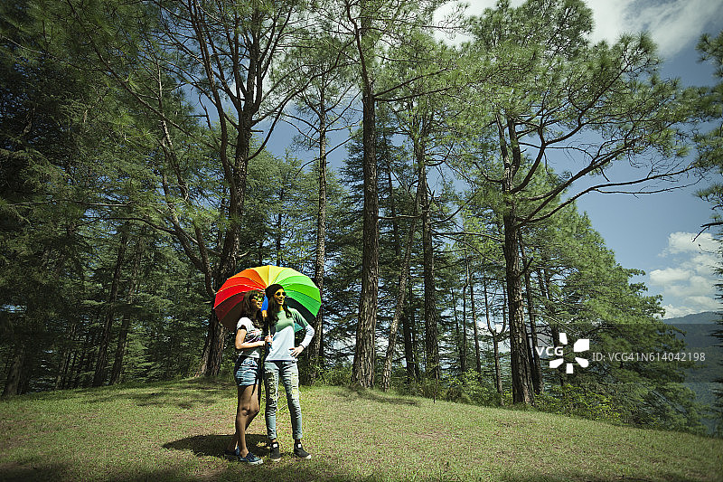 两个快乐的亚洲青少年朋友站在雨伞下的自然。图片素材