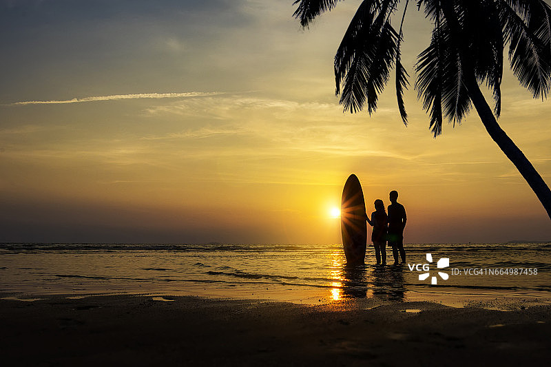 夕阳西下的海滩上，男人和女孩带着冲浪板图片素材