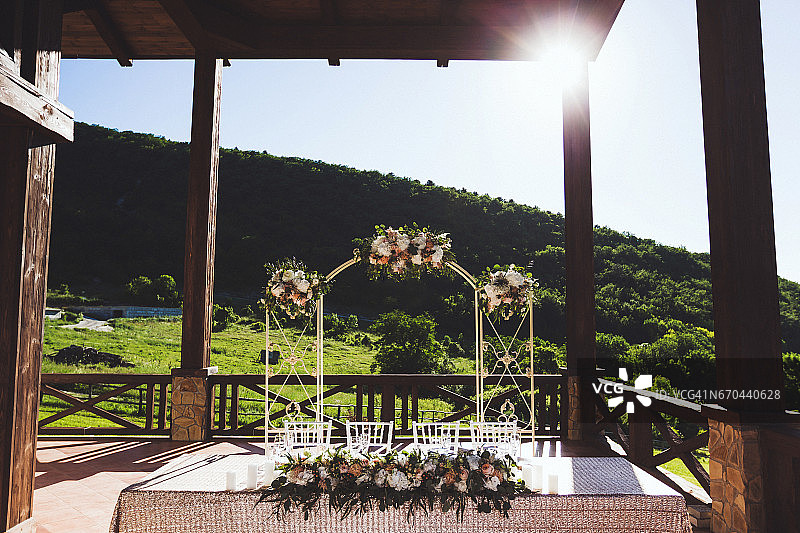 装饰漂亮的婚宴室外大阳台。阳光下，白色的桌子和拱形的鲜花图片素材